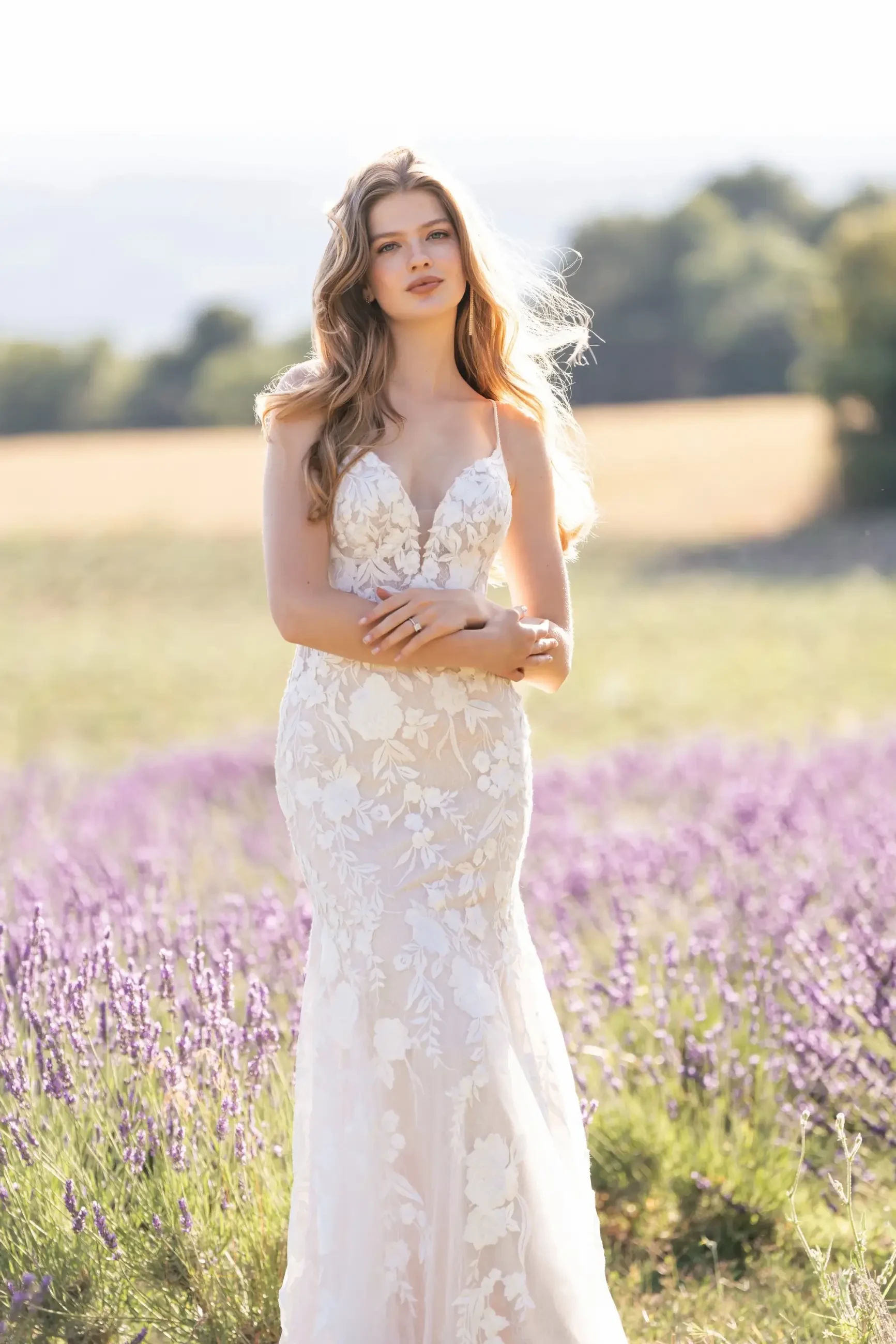 Model is wearing a Chantilly lace sheath gown adorned with trailing lace appliqués in the shape of vines and blossoms.