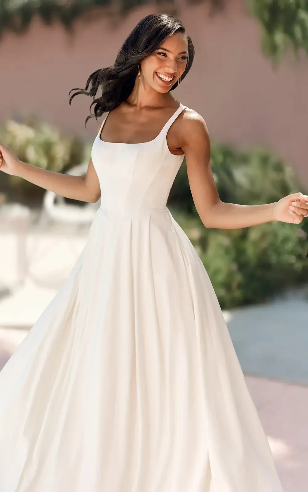 A woman smiling while wearing a white dress, twirling in a bright outdoor setting.